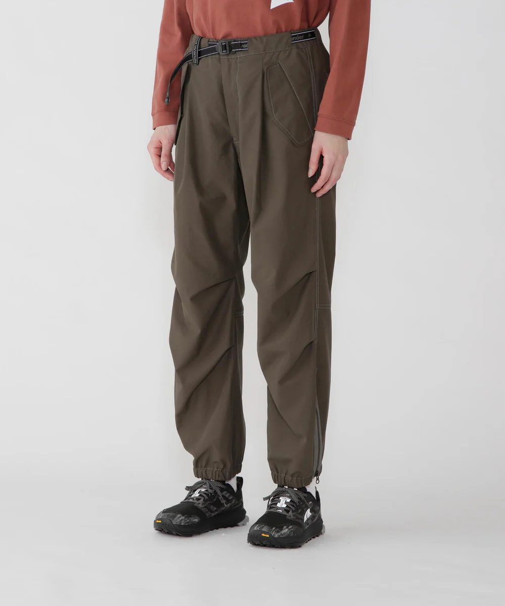 Pantalon utilitaire and wander kaki, coupe légèrement ample avec poches fonctionnelles et chevilles resserrées, associé à des sneakers techniques, illustrant l’esthétique gorpcore japonaise entre performance et minimalisme.