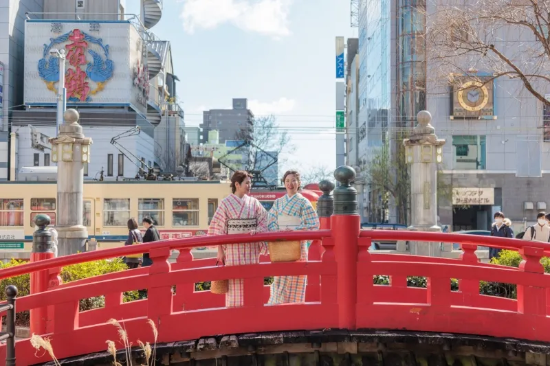 Deux femmes portant des yukatas de la boutique Gofuku Ishihara sur un pont rouge au Japon.
