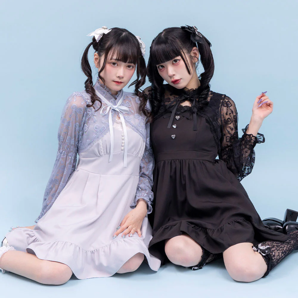 Dos jóvenes posando con vestidos Lolita en colores pastel y negro, con detalles de encaje y lazos. Están sentadas sobre un fondo azul claro que resalta la elegancia de sus atuendos.
