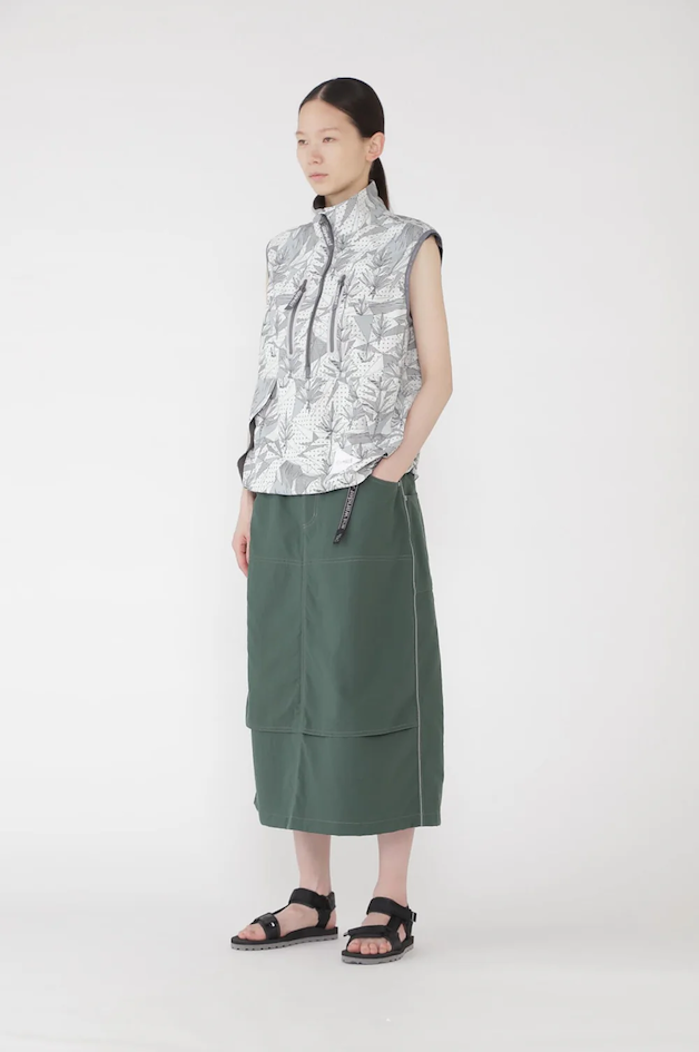 Jupe technique longue vert foncé associée à un gilet outdoor zippé à imprimé graphique et sandales techniques, illustrant l’alternative au pantalon gorpcore japonais.