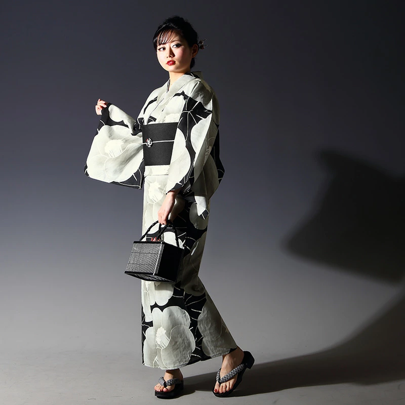 Femme portant un yukata noir et blanc à grands motifs floraux, avec obi noir, geta et petit sac assorti.