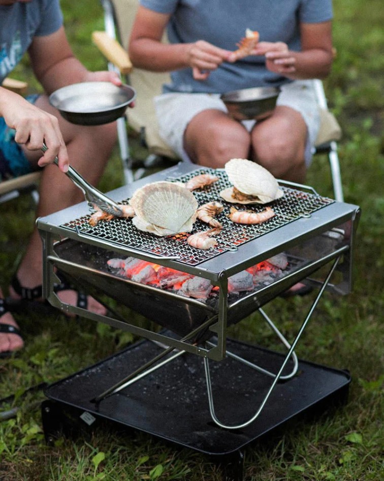 Barbecue pliable Snow Peak Takibi Grill avec grillage et braises, utilis&eacute; en camping pour cuire fruits de mer et aliments en ext&eacute;rieur