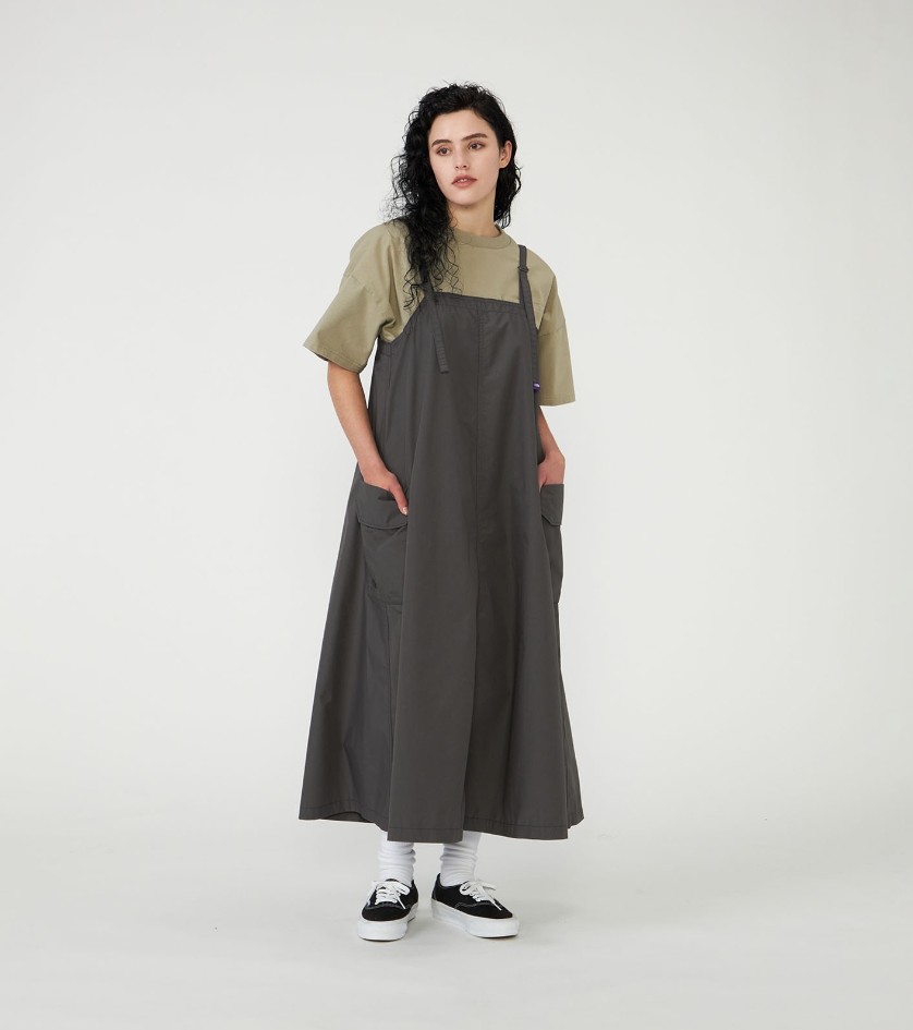 Femme portant une tenue gorpcore composée d’une robe longue ample gris anthracite superposée à un t-shirt beige, avec chaussettes blanches et baskets noires.
