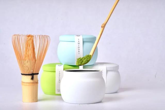 Dos sobres metálicos de matcha verde en polvo, acompañados de un recipiente cilíndrico de almacenamiento.