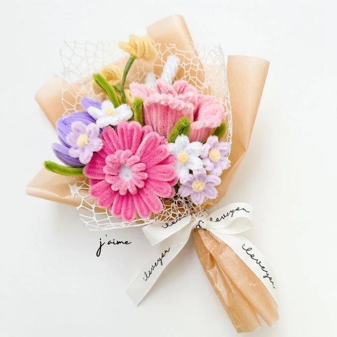 Ramo de flores artificiales en tonos púrpura y rosa, con tallos envueltos y cinta decorativa.