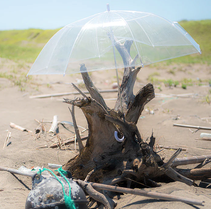 imagem de um guarda chuva de pl&aacute;stico no meio da praia, causando polui&ccedil;&atilde;o