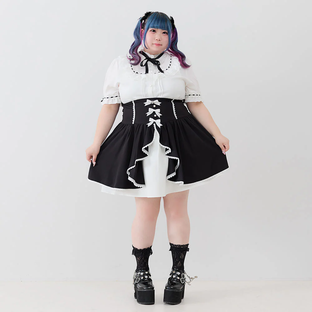 Modelo usando un vestido Jirai en blanco y negro con corset decorativo. Complementa el look con medias de encaje, plataformas negras y un peinado colorido con tonos azules y morados.
