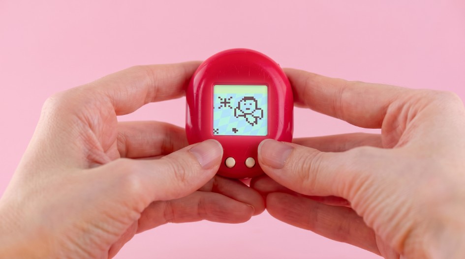 Two hands holding a red Tamagotchi.