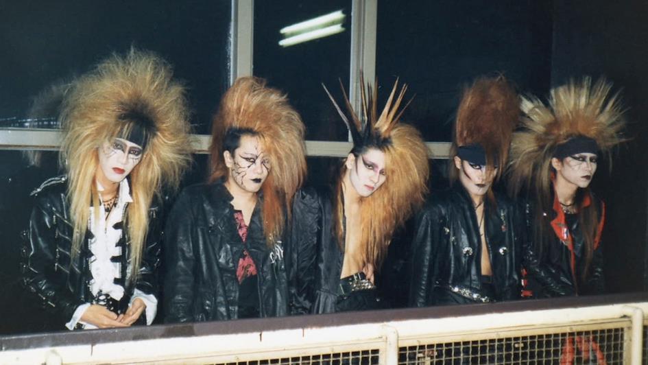 Les membres de X Japan arborant coiffures volumineuses et maquillage scènique typique du visual kei, image extraite d'un documentaire