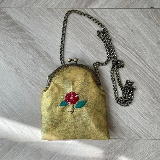 Bolso rectangular de seda con bordado floral, broche metálico y correa ajustable para llevar al hombro.